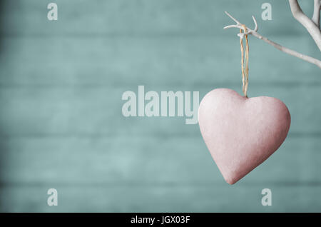 Un coeur peint rose, suspendu à partir de la branche de l'arbre artificiel blanc, avec la planche en bois turquoise pâle d'arrière-plan flou. Des teintes pastel. Banque D'Images