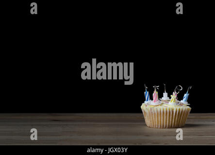 Un anniversaire cupcake papier ordinaire dans un cas avec sept bougies à rayures qui ont incendié et été soufflées. Placé sur une table en bois avec black b Banque D'Images