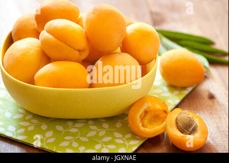 Abricot savoureux avec des feuilles se situent sur une planche de bois. Tas d'abricots en bol en bois sur la table Banque D'Images