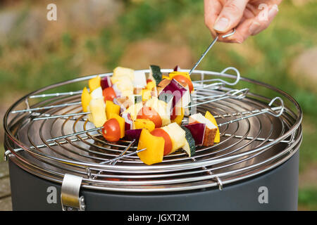 Homme met des kebabs vegan avec légumes et tofu sur un gril de table. Banque D'Images