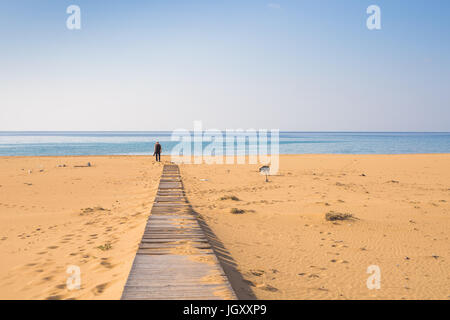 Homme avec chien marcher sur le chemin en bois sur la plage et à la recherche dans la distance de l'océan Banque D'Images