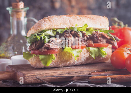 Sandwich au bœuf à la tomate et salade sur planche à découper en bois avec des ingrédients. Banque D'Images