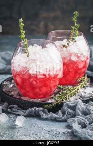 Verre rouge avec berry, la glace et le thym. Cocktail d'été rafraîchissante dans un verre sur fond gris Banque D'Images