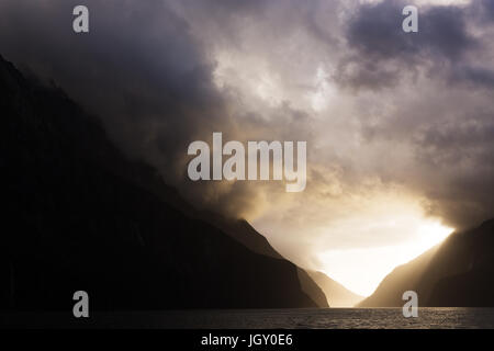 Flux lumineux de la lumière du soleil à travers les nuages de tempête menaçante comme on suspend sur majestueux pics enneigés, de l'éclairage d'un chemin à travers les montagnes en couches. Banque D'Images