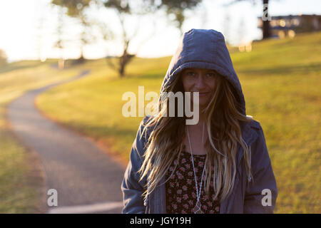 Une jeune fille portant un avec capuchon sur un sentier lumineux dans un parc de la ville. Banque D'Images