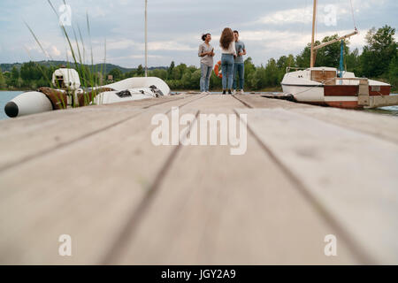 Trois amis sur la jetée, à côté de la voile, relaxant, holding de bouteilles de bière, low angle view Banque D'Images