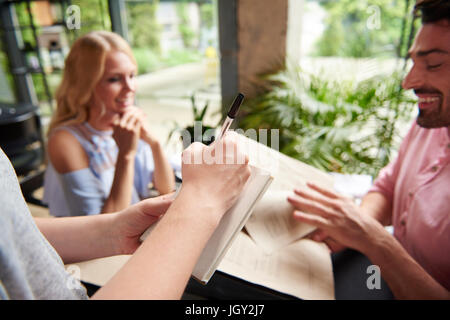 Plus d'épaule de serveuse afin d'écriture de couple at restaurant table Banque D'Images