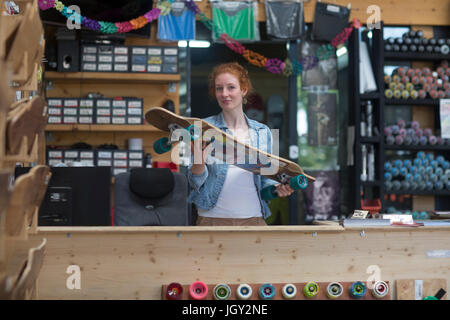 Portrait de femme en skateboard shop, holding skateboard Banque D'Images