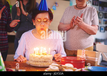 Senior woman blowing out candles on cake at Birthday party Banque D'Images