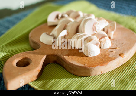 Le processus de la coupe champignon champignons sur une planche à découper en bois sur fond de tissu vert close-up Banque D'Images