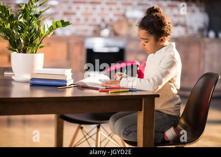 Vue latérale du cute african american girl sitting at table et faire leurs devoirs Banque D'Images