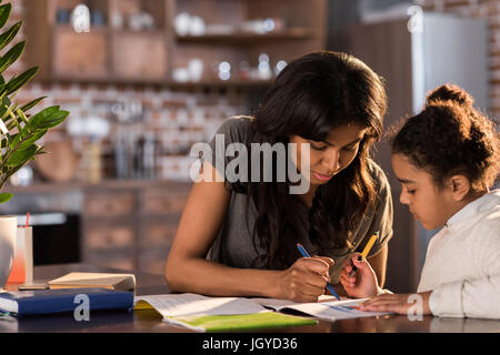 Mère et sa fille peu cute assis à table et faire leurs devoirs ensemble à la maison, concept d'aide aux devoirs Banque D'Images