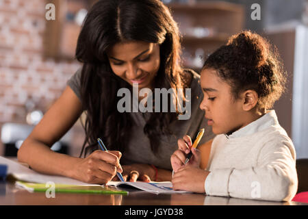 Mère et sa fille peu cute assis à table et faire leurs devoirs ensemble à la maison, concept d'aide aux devoirs Banque D'Images