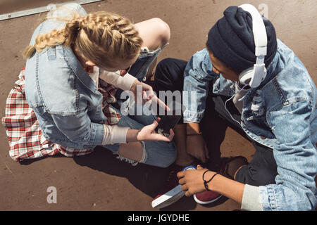 Couple hipster écoutant de la musique avec des écouteurs et siiting dans un planchodrome, les adolescents s'amusant concept Banque D'Images