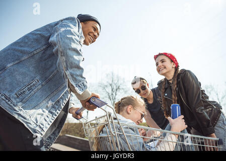 Groupe d'adolescents souriants s'amusant avec panier à skateboard park Banque D'Images