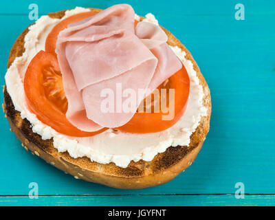 Jambon et fromage tomate bagel sésame contre un fond bleu Banque D'Images