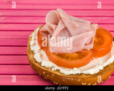 Jambon et fromage tomate bagel sésame contre un fond rose Banque D'Images