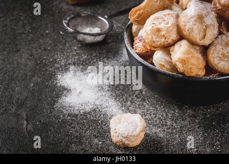 La cuisson à la maison, les feuilletés. La nourriture à la mode. Cronuts popcorn, puff, trous de beignes dans un bol noir et un sac en papier, avec du sucre en poudre. Sur une pierre sombre Banque D'Images