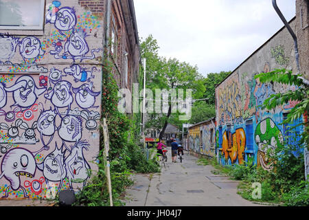 Deux personnes à pied leurs vélos à travers une ruelle remplie de street art / graffiti dans la zone Friedrichshain de Berlin, Allemagne Banque D'Images