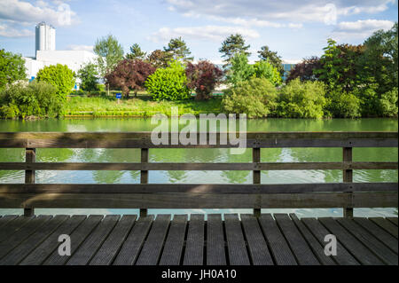 Un ponton en bois avec rampes en bois en face d'une rivière avec des arbres et de la végétation sous un ciel bleu avec des nuages blancs. Banque D'Images