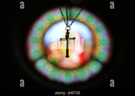 Crucifix suspendu contre la lumière sur un vitrail. Eglise Saint Clodoald. Saint-Cloud. Banque D'Images