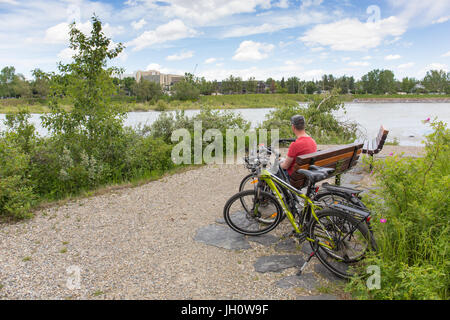 Un homme est assis sur un banc dans le parc Edworthy avec deux vélos à côté de lui le long de la rivière Bow, à Calgary, Alberta, Canada Banque D'Images