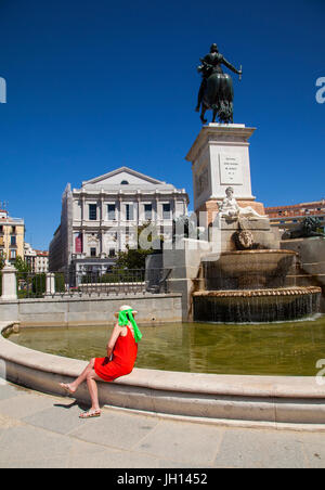 Femme dans une robe rouge assis en face du Teatro Real / Theatre Royal et le monument à Felipe IV à Madrid Espagne Banque D'Images