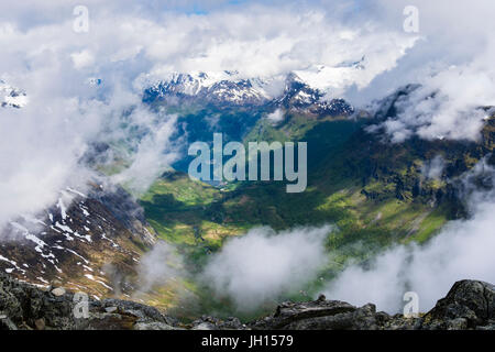 Vue vers le bas à travers les nuages de Geirangerfjorden avec montagnes aux sommets enneigés de la montagne Dalsnibba en été. Geiranger, Norvège Banque D'Images