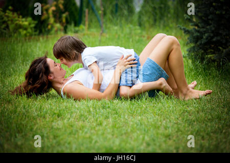 Belle jeune femme enceinte et son enfant plus âgé, couché dans l'herbe, faisant des bulles de savon dans le jardin Banque D'Images