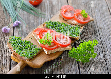 Snack-végétarien : tranches de pain de campagne beurrée avec de la ciboulette fraîche et les tomates sur une planche en bois Banque D'Images