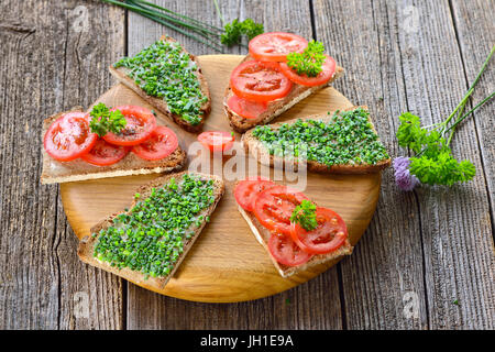 Snack-végétarien : tranches de pain de campagne beurrée avec de la ciboulette fraîche et les tomates sur une planche en bois Banque D'Images