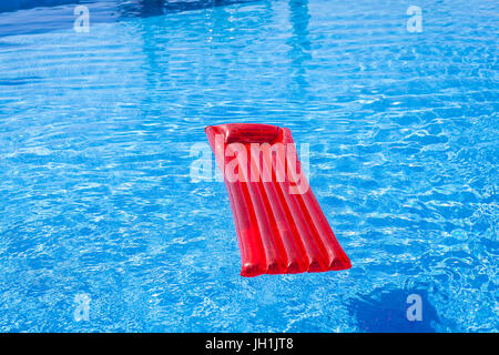 Chaise longue gonflable rouge lilo floating in a swimming pool Banque D'Images