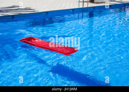 Chaise longue gonflable rouge lilo floating in a swimming pool Banque D'Images