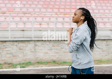 Portrait de l'athletic côté afro-American girl du jogging le long du stade tout en écoutant de la musique dans les écouteurs. Banque D'Images