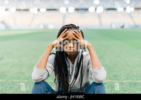 Close-up portrait de l'afro-american sportgirl assis sur l'herbe et s'appuyant sur les genoux. Banque D'Images