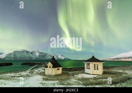 Les aurores boréales et les étoiles illuminent les huttes de bois par la mer de glace, Djupvik, Alpes de Lyngen, Troms, Norvège Banque D'Images