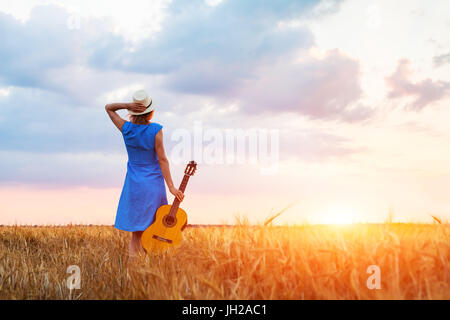 Musicien avec sa guitare femme dans les champs à la recherche au coucher du soleil, l'été chaud à l'extérieur Banque D'Images