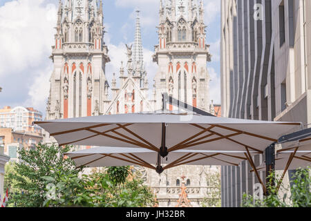 Bâtiment moderne avec un grand parapluie du café avec une terrasse donnant sur l'ancienne façade de l'église catholique médiévale sur un arrière-plan. Banque D'Images