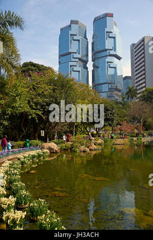 Les gens qui marchent autour d'un lac à Hong Kong Park entouré de grands immeubles de bureaux à Hong Kong, Chine. Banque D'Images