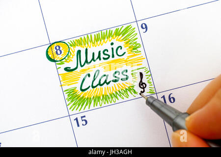 Les doigts de femme à la plume l'écriture dans la classe de musique rappel calendrier. Banque D'Images