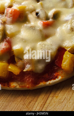 Un mélange de légumes végétarien pizza, garnie de fromage mozzarella fondu et photographié d'en haut sur une planche à découper en bois rayé. Banque D'Images