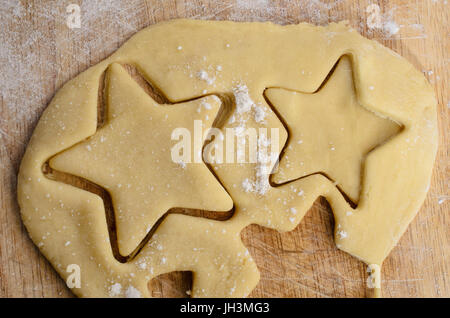 Pâte à biscuit roulé avec des formes étoiles vut à partir de la pâte sur une surface farinée ancienne en bois planche à découper. Banque D'Images