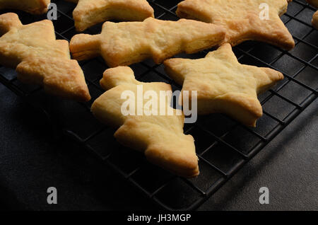 Arbre généalogique de boulangerie juste et star shaped Christmas biscuits (cookies), circuit de refroidissement sur un fil noir rack après la sortie du four. Plan de cuisine noir ci-dessous. Banque D'Images