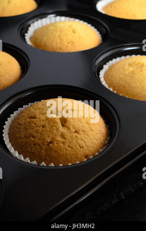 Un petit pain fraîchement cuit au four d'étain rempli de petits gâteaux à la vanille d'or en cas de papier, de refroidissement sur l'ardoise noire. Banque D'Images