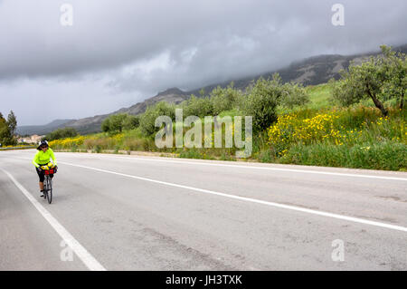 Une randonnée cycliste féminin sur une route de campagne et les nuages se profilent derrière elle en Sicile, Italie. Banque D'Images