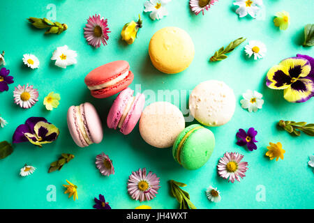 Macarons colorés et appétissants de belles fleurs sur fond vert. Modèle plat Banque D'Images