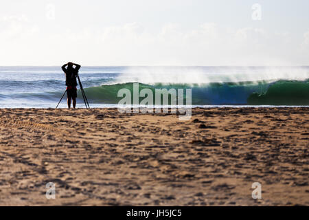 Un photographe regarde de la plage comme un internaute reçoit sur une vague parfaite susceptible, grâce à un spot de surf en Australie. Banque D'Images