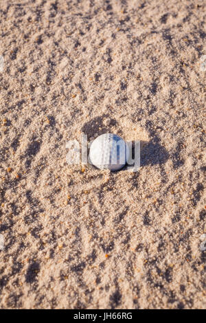 Balle de golf dans le sable d'un bunker sur terrain de golf sur une journée ensoleillée Banque D'Images