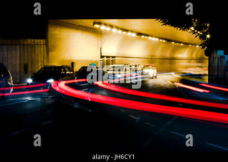 Le trafic de nuit dans les rues de la ville. Les voitures d'attente à la sortie du tunnel, à l'intersection d'attente alors que la conduite de véhicules déménagement passé laissant couleur light trails Banque D'Images