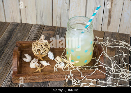 Verre de limonade dans polka dot pot Mason de paille à rayures avec les coquillages sur le plateau de service en bois Banque D'Images
